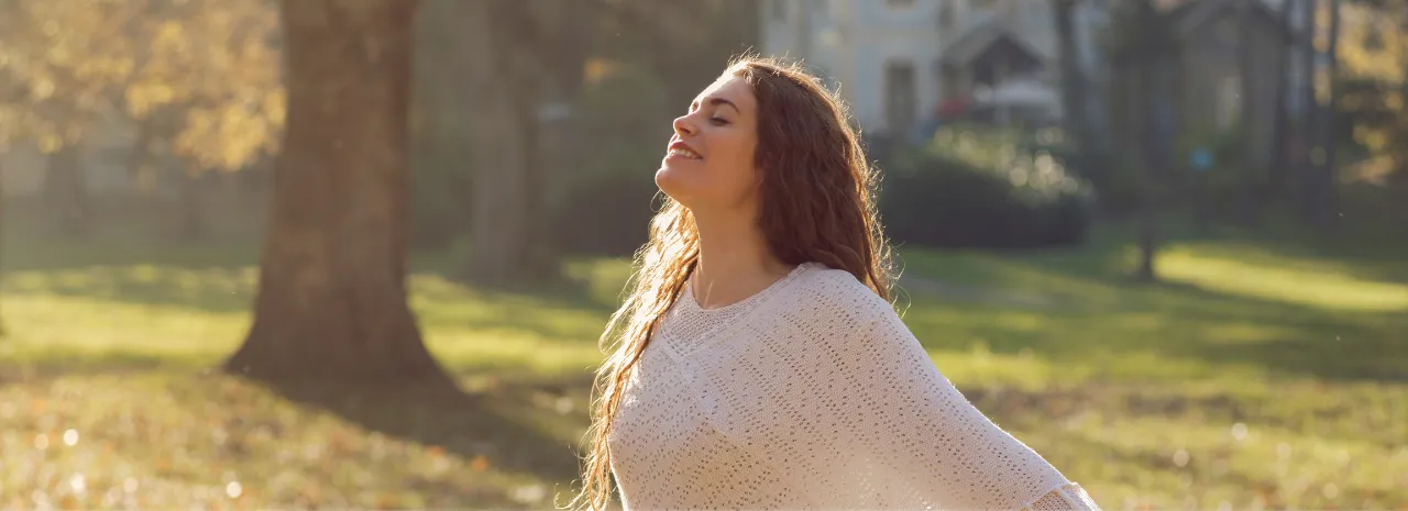 A woman smiling in the sunshine, arms open